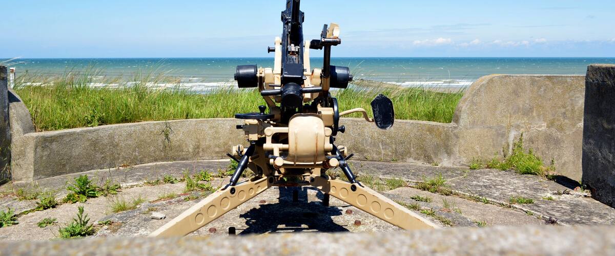 A mounted machine gun on a concrete platform overlooking the ocean.