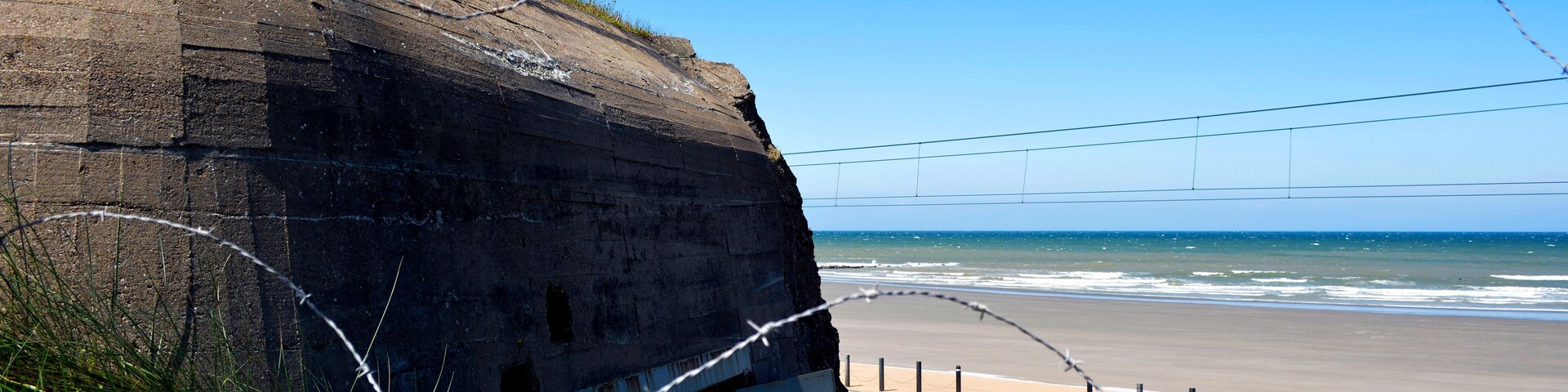 Una carretera costera con una cerca de alambre de púas, una playa y el océano al fondo.