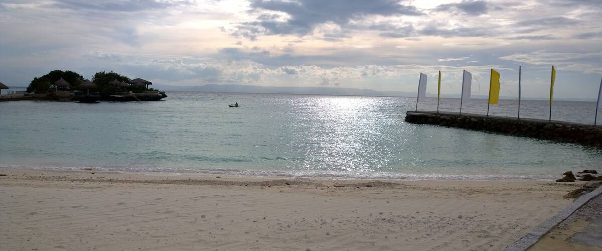 A beach with a calm sea, a rocky outcrop, and a row of flags.