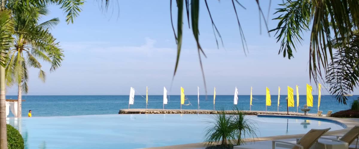 A pool with lounge chairs, palm trees, and flags by the ocean.