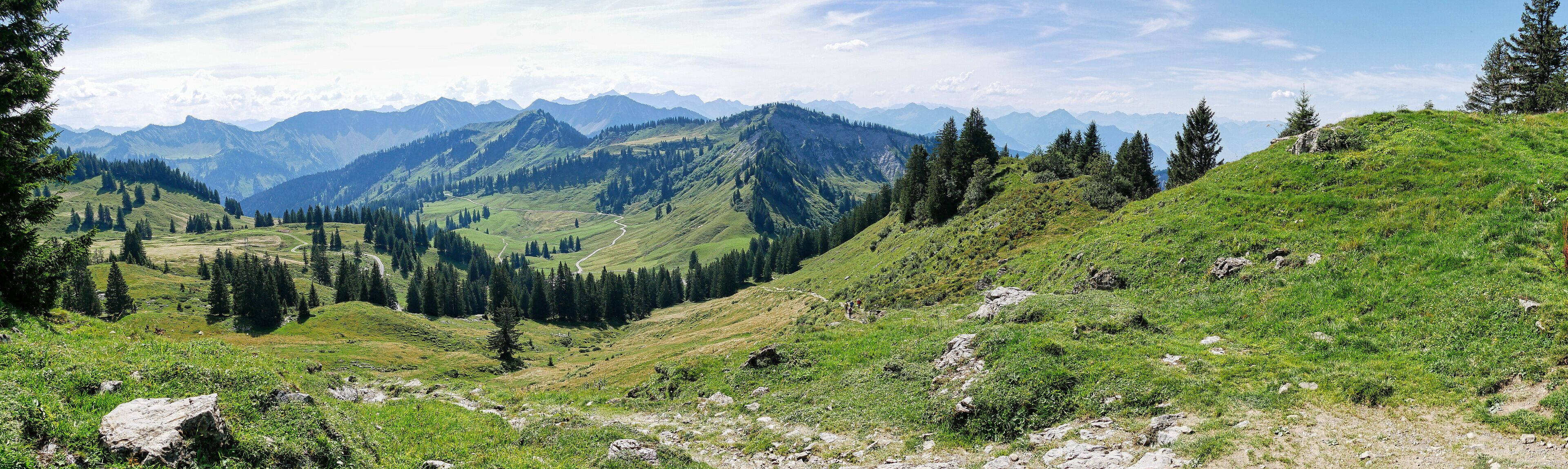 A mountainous landscape with a winding road, dense forests, and distant peaks.