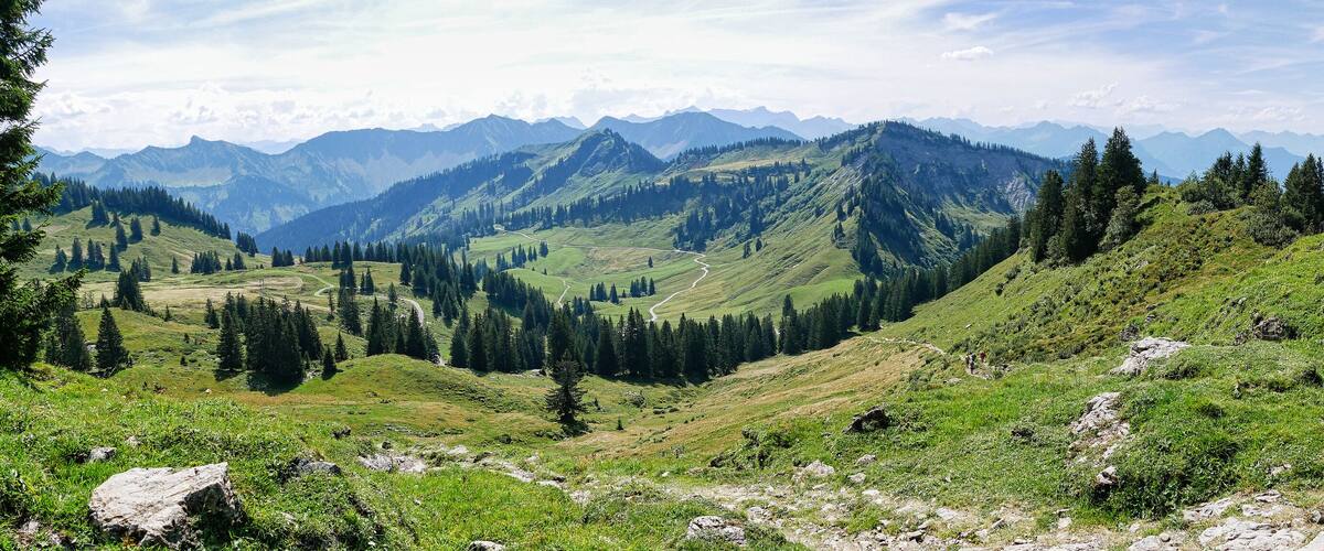 A mountainous landscape with a winding road, dense forests, and distant peaks.