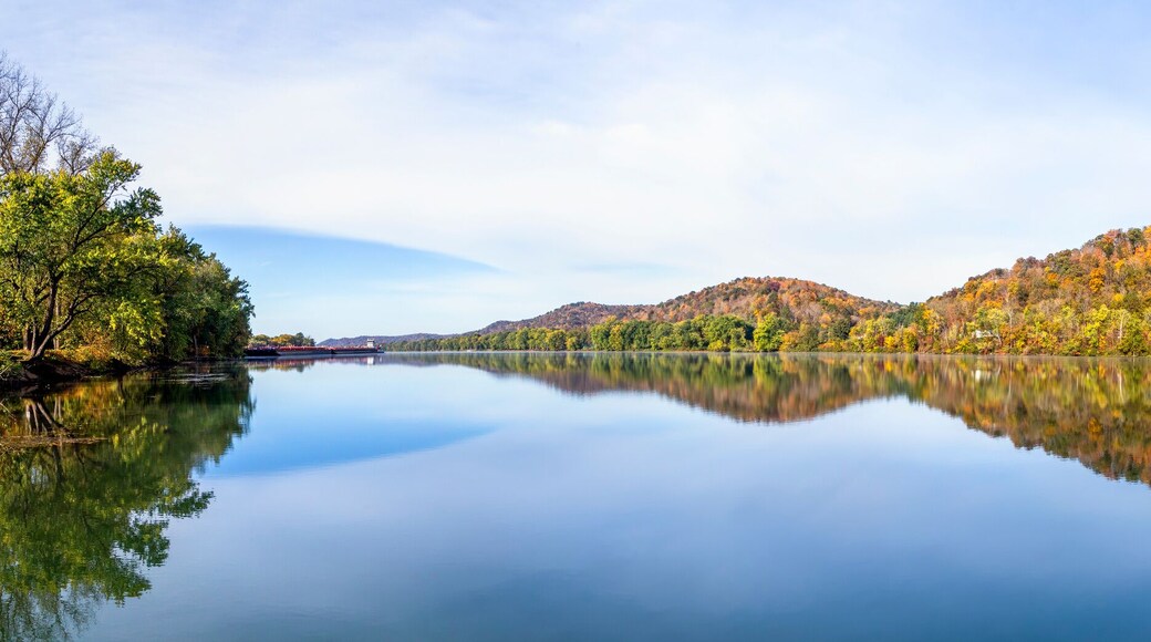 Hills covered in colorful fall foliage are reflected on the still water of the beautiful Ohio River. Monroe County, Ohio is viewed from the river bank at Paden City, West Virginia.