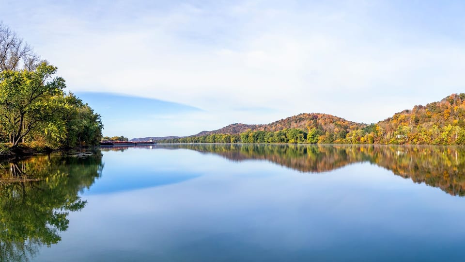 A calm lake reflecting autumn-colored trees and hills.