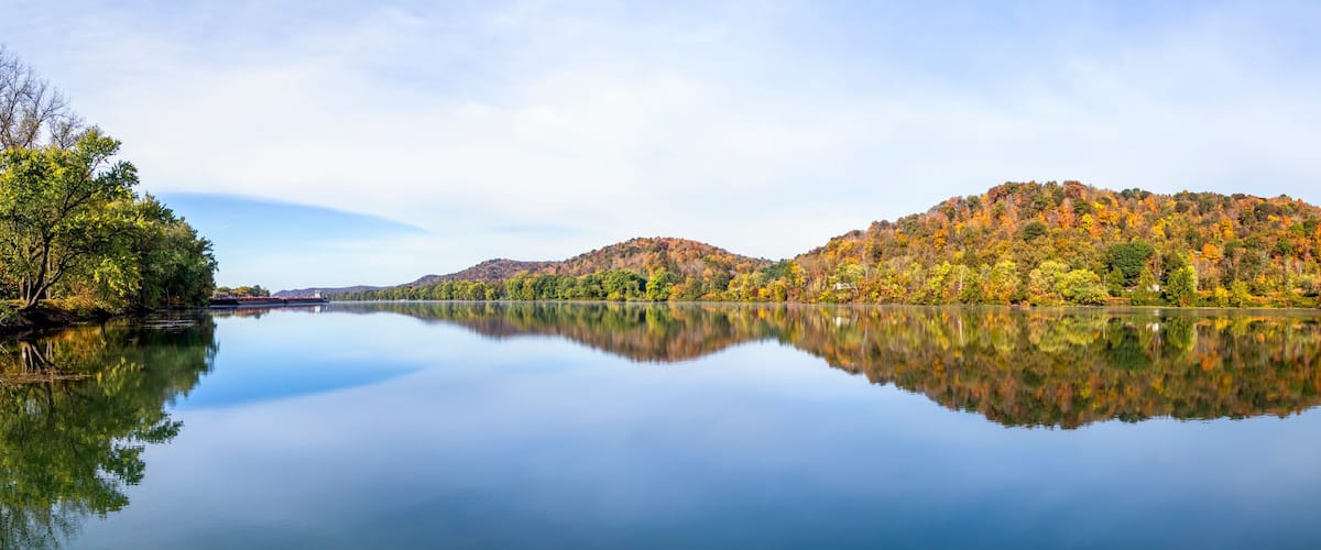 A calm lake reflecting autumn-colored trees and hills.