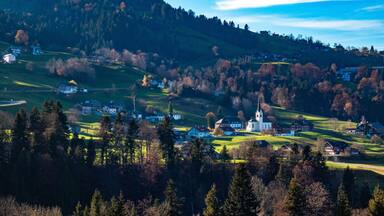 A village with a church on a hill, surrounded by trees and houses.