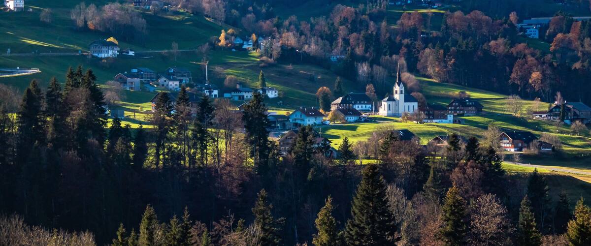 A village with a church on a hill, surrounded by trees and houses.