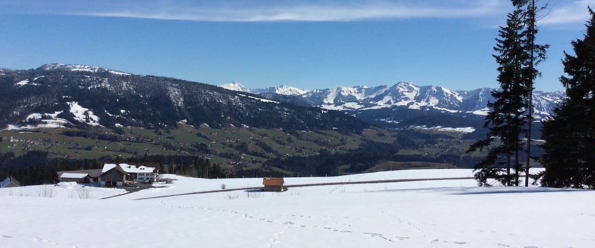 A snowy mountain landscape with a clear blue sky, a wooden cabin, and a snow-covered field.