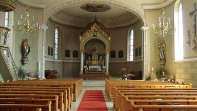 An ornate church interior with wooden pews, a red carpet, and religious statues.
