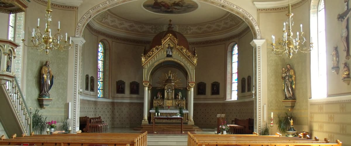 An ornate church interior with wooden pews, a red carpet, and religious statues.