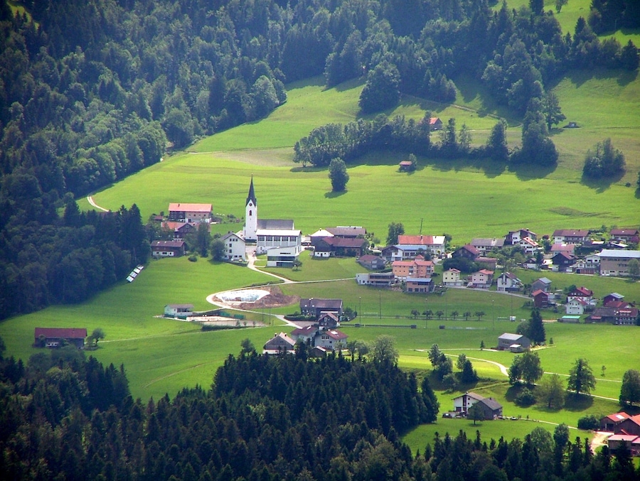 Ein Dorf mit einer Kirche, umgeben von grünen Feldern und Bäumen.