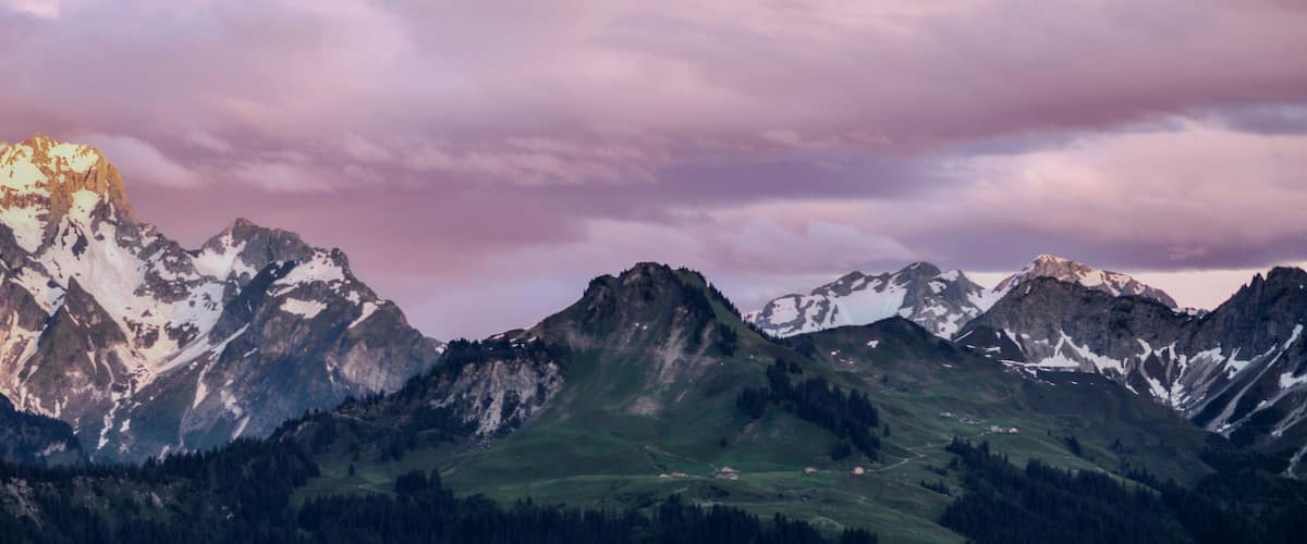 A mountain range with snow-capped peaks and a valley with scattered houses.
