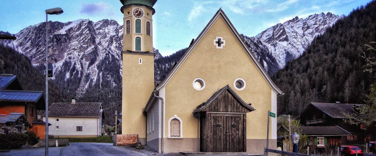 A church with a clock tower and a mountain backdrop.