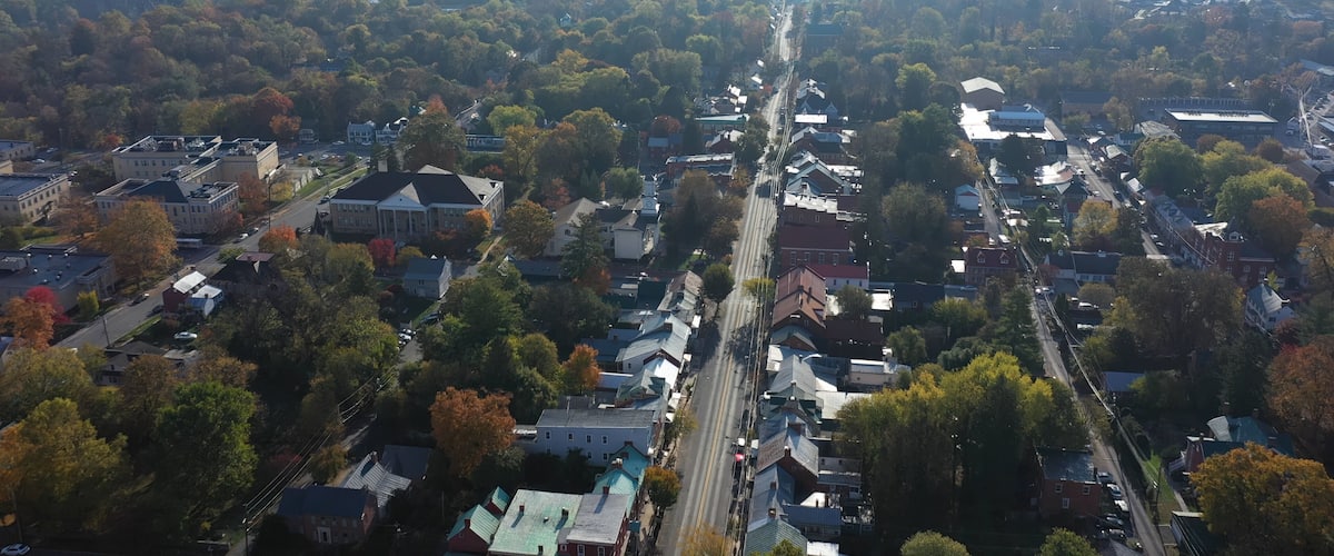 An aerial view of a town with a river, dense trees, and various buildings.
