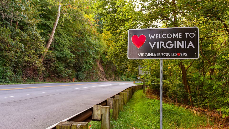 A road bordered by a wooden guardrail and a sign welcoming visitors to Virginia.