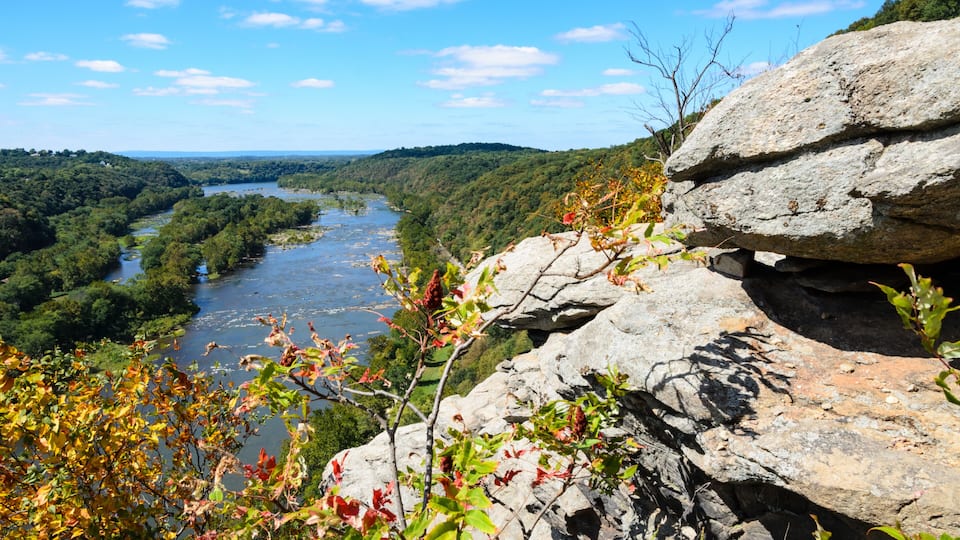 A river valley with dense foliage, a prominent rock formation, and a clear blue sky.