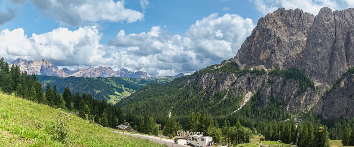 A mountainous landscape with a road, a sign reading "CALFOSTEL", and a cable car system.