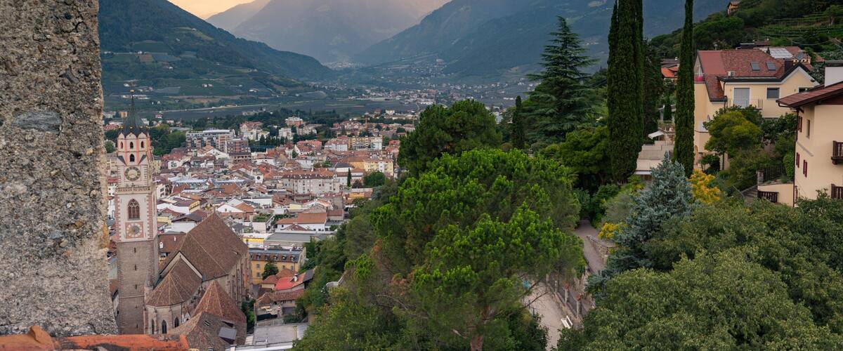 A town nestled in a valley with mountains in the background, a prominent church, and a mix of residential and commercial buildings.