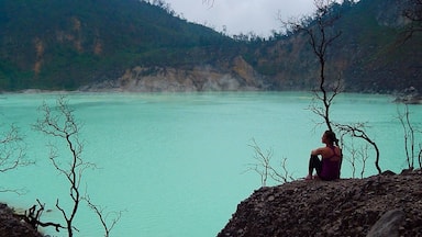 Una persona sentada sobre un afloramiento rocoso con vistas a un lago turquesa y montañas al fondo.