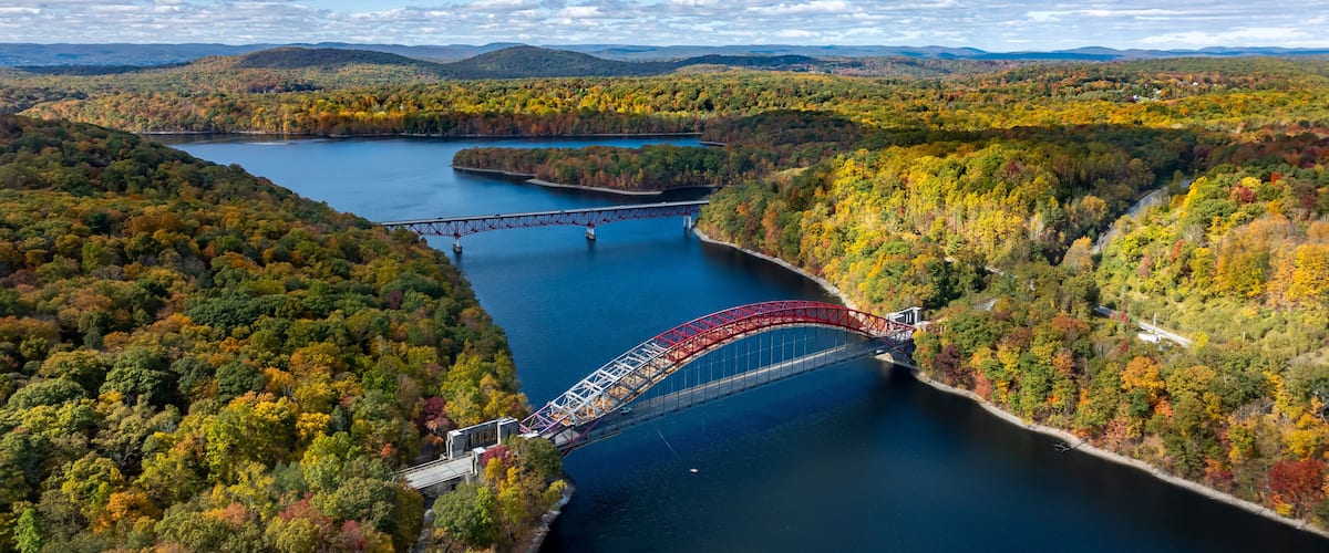 A red bridge over a river surrounded by autumn foliage.
