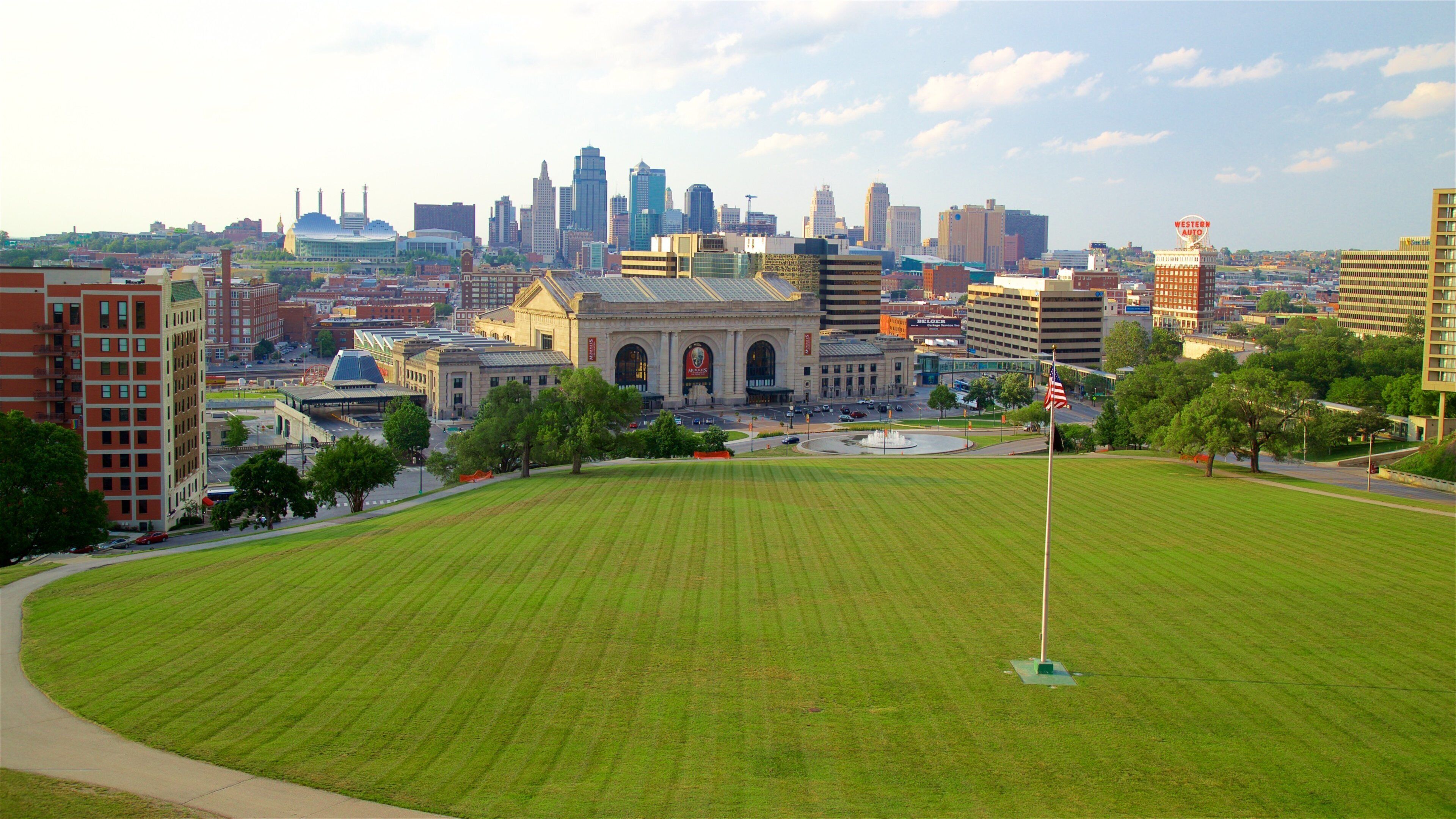A cityscape with a large green field, historic buildings, and a modern skyline.