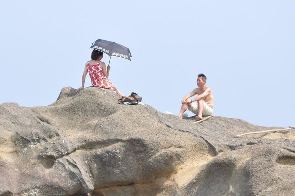 Two people sitting on a rocky hill with an umbrella.