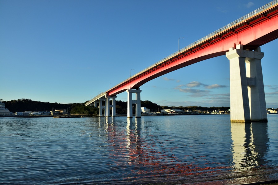 A red bridge over calm water with a clear sky.