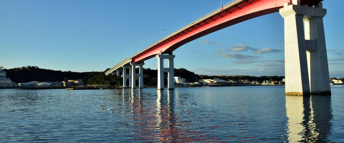 A red bridge over calm water with a clear sky.