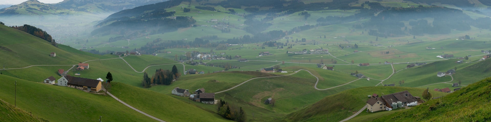 A mountainous landscape with rolling green hills, scattered houses, and a village nestled among the valleys.