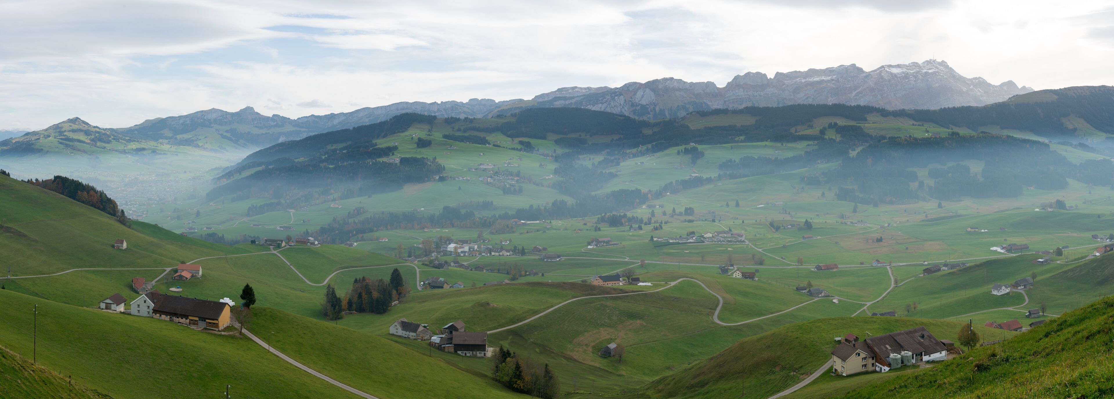 A mountainous landscape with rolling green hills, scattered houses, and a village nestled among the valleys.