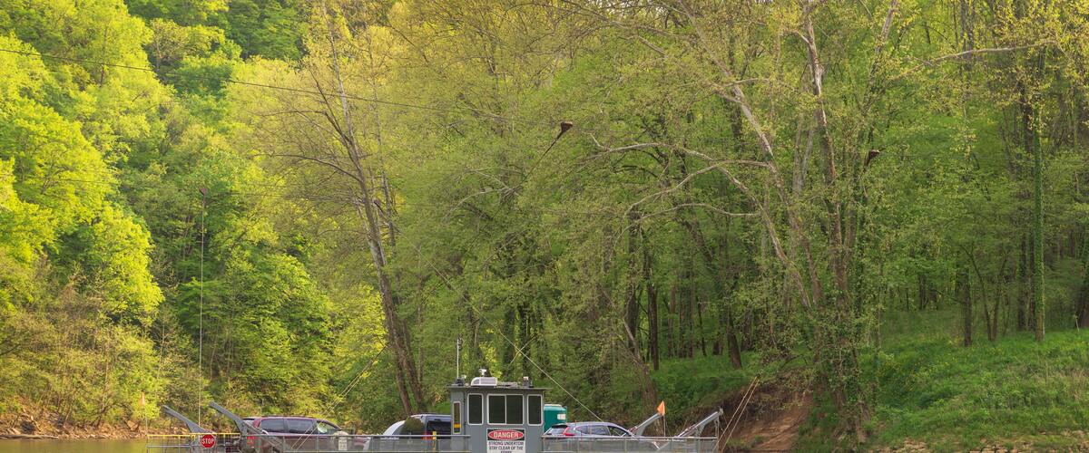 A riverboat docked near a forested area with a warning sign.