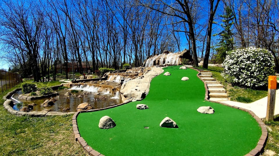 A miniature golf course with a green putting surface, a small pond, and a waterfall.