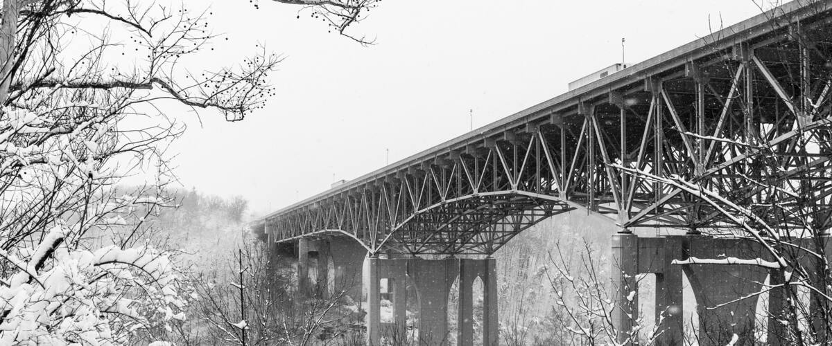 A snow-covered railway bridge with bare trees in the foreground.