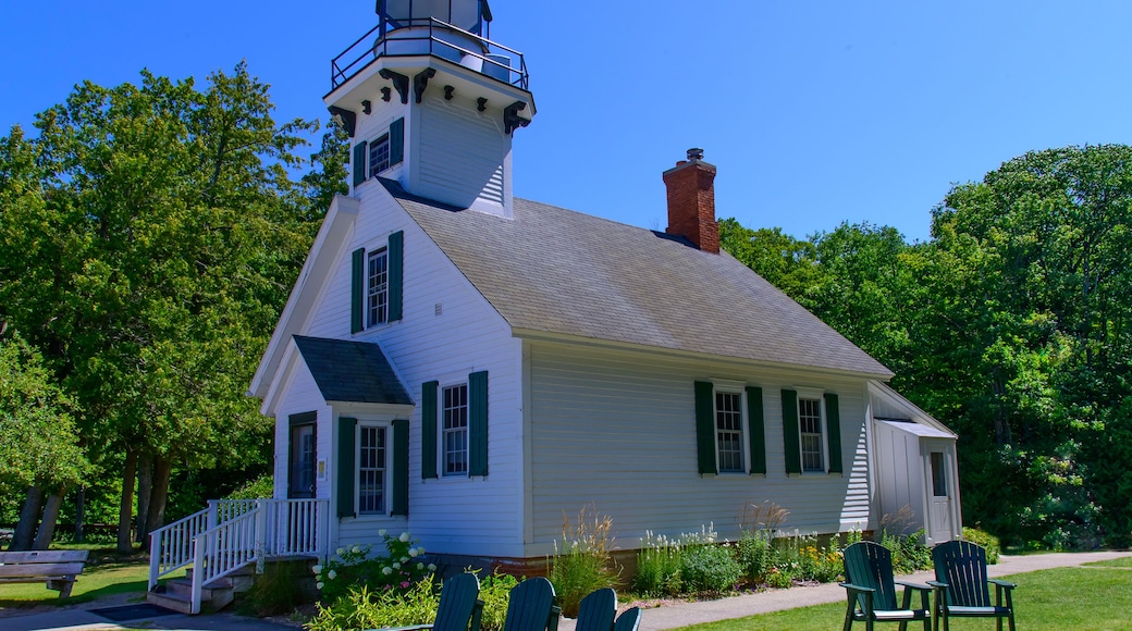 Un phare blanc avec des volets verts, une cheminée en briques et un porche blanc agrémenté de chaises Adirondack.