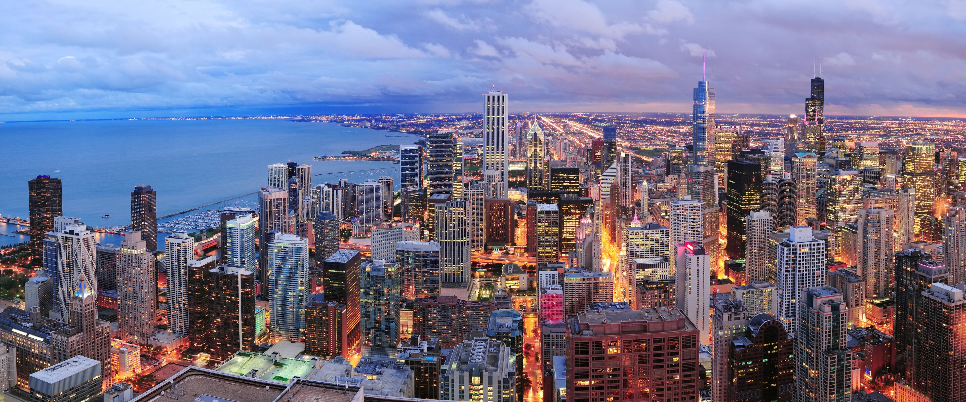 A densely packed cityscape with numerous high-rise buildings, a large body of water in the background, and a bridge connecting two land masses.