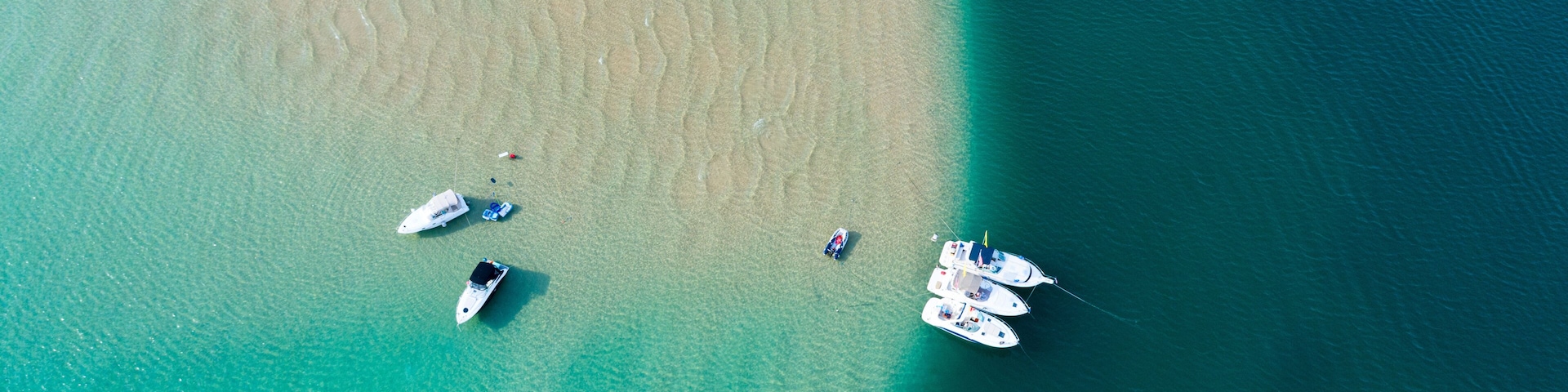 Aerial view of boats anchored on a sand bar in crystal clear blue water.