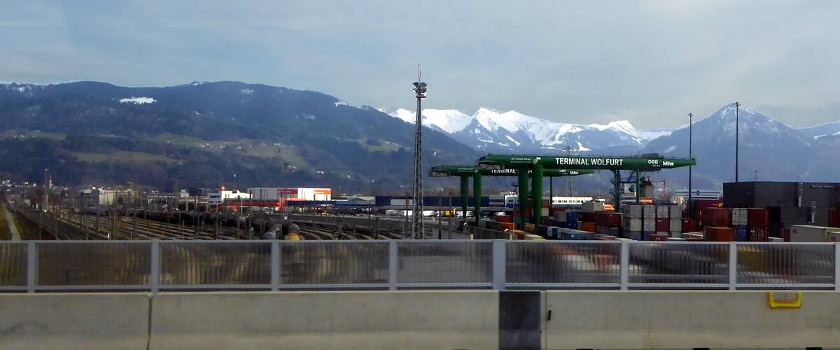 A railway station with a sign reading "TERMINAL WOLFURT" and mountains in the background.