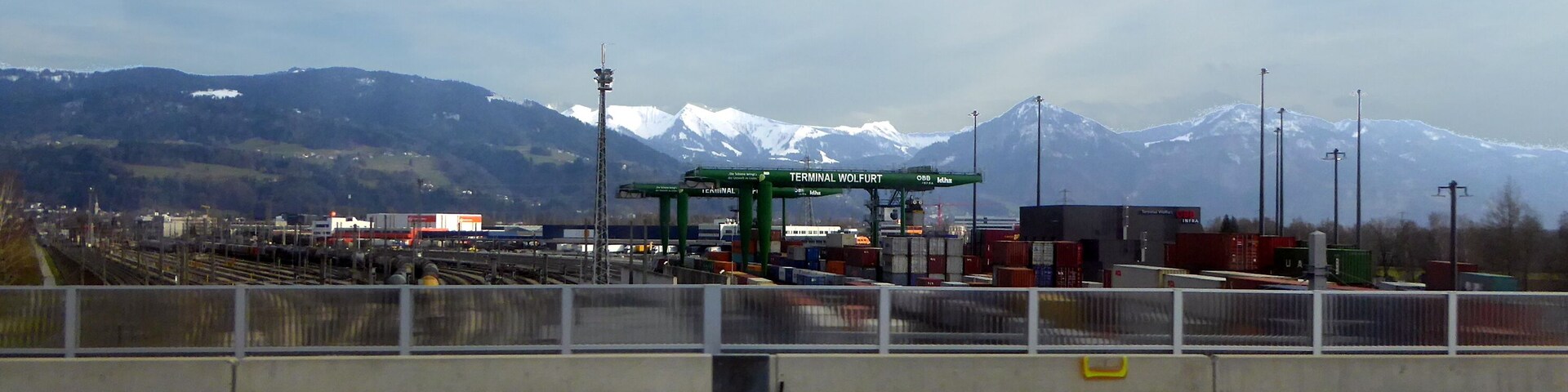 A railway station with a sign reading "TERMINAL WOLFURT" and mountains in the background.