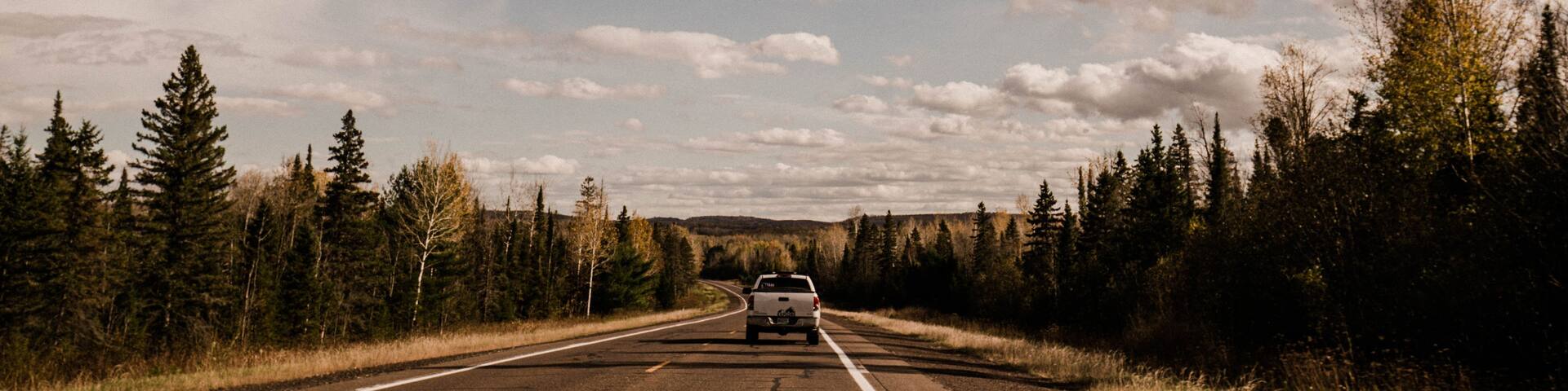 A road with a vehicle, surrounded by trees and a cloudy sky.