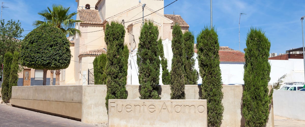 A church with a clock tower and a sign reading "Fuente Alamo".