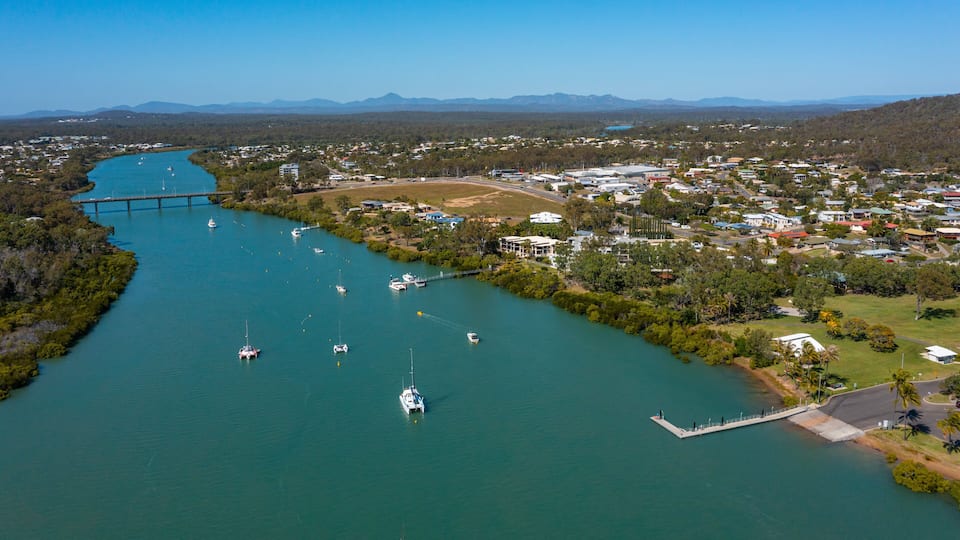 A river with boats, a bridge, and a town with houses and greenery.