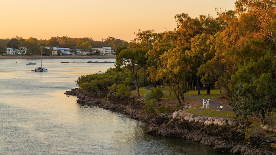 A coastal landscape with a rocky shoreline, a park with a walking path, and houses in the background.