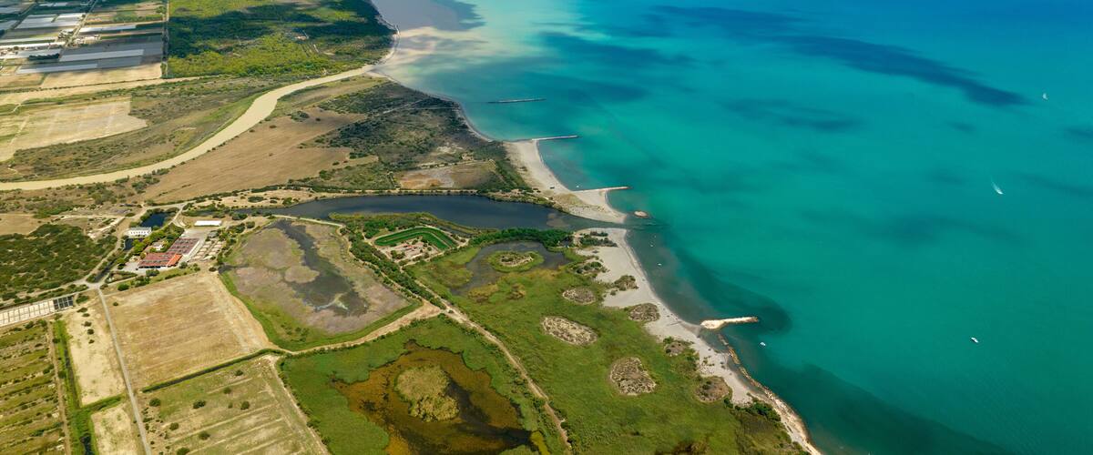 An aerial view of a coastal area with a river, green fields, and a beach.