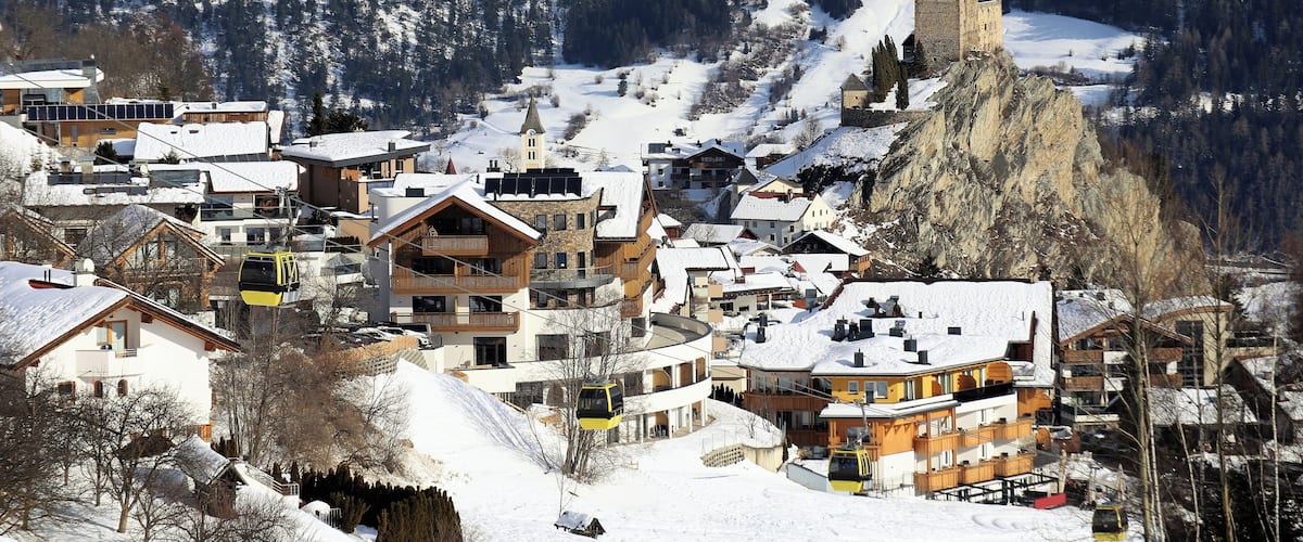 A snow-covered village with buildings, a ski lift, and a castle on a mountain.