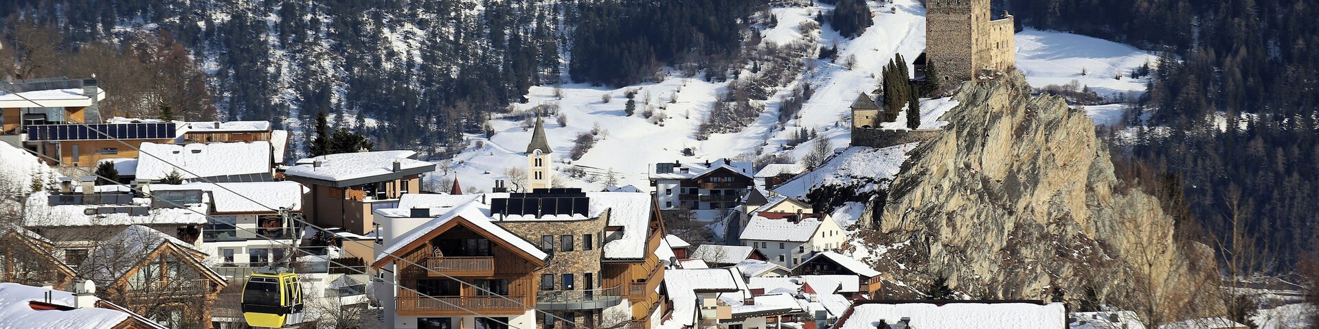 A snow-covered village with buildings, a ski lift, and a castle on a mountain.