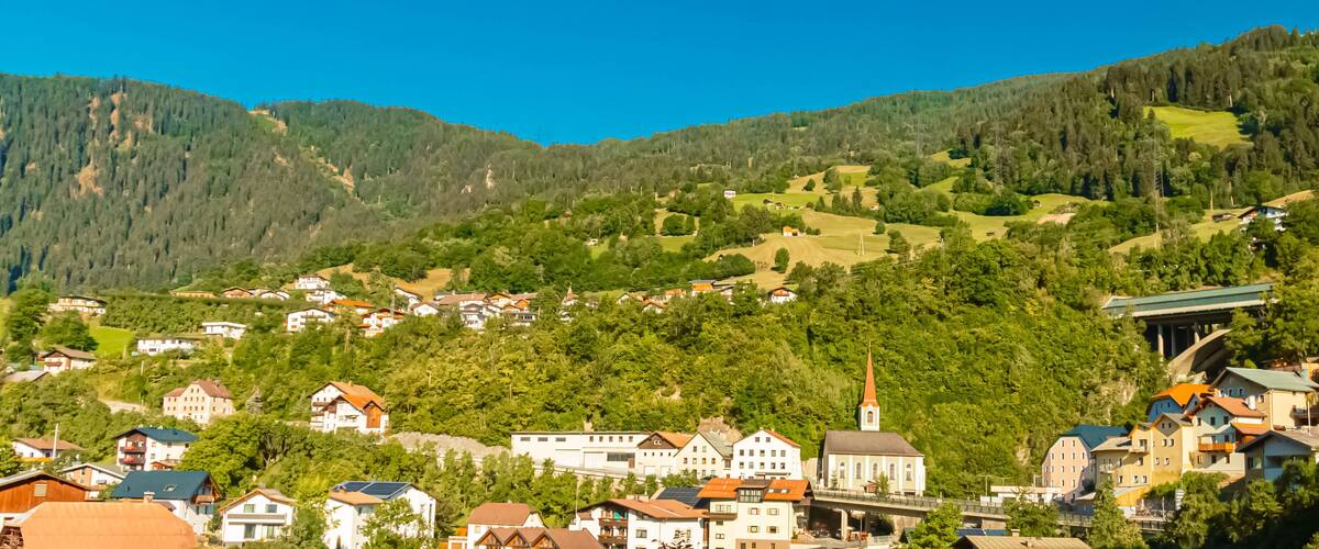 A village nestled in a valley with a church and houses surrounded by lush green hills.