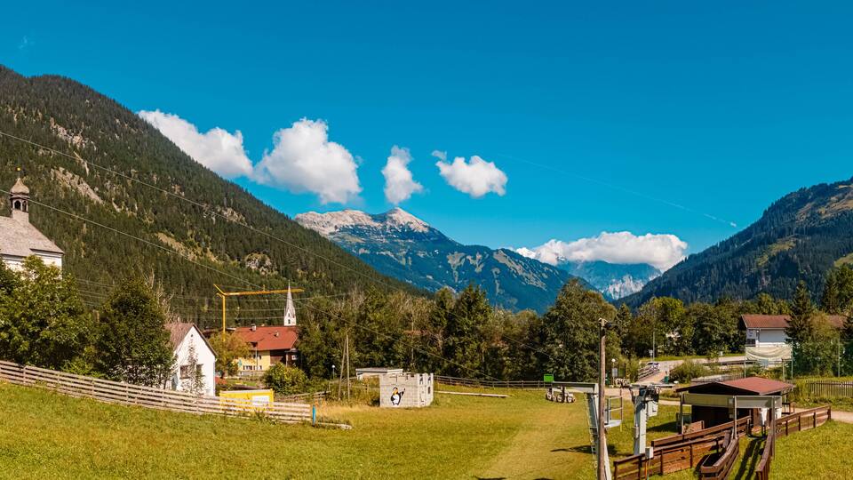 A mountain village with a church, a ski lift, and a fenced area with a small building.