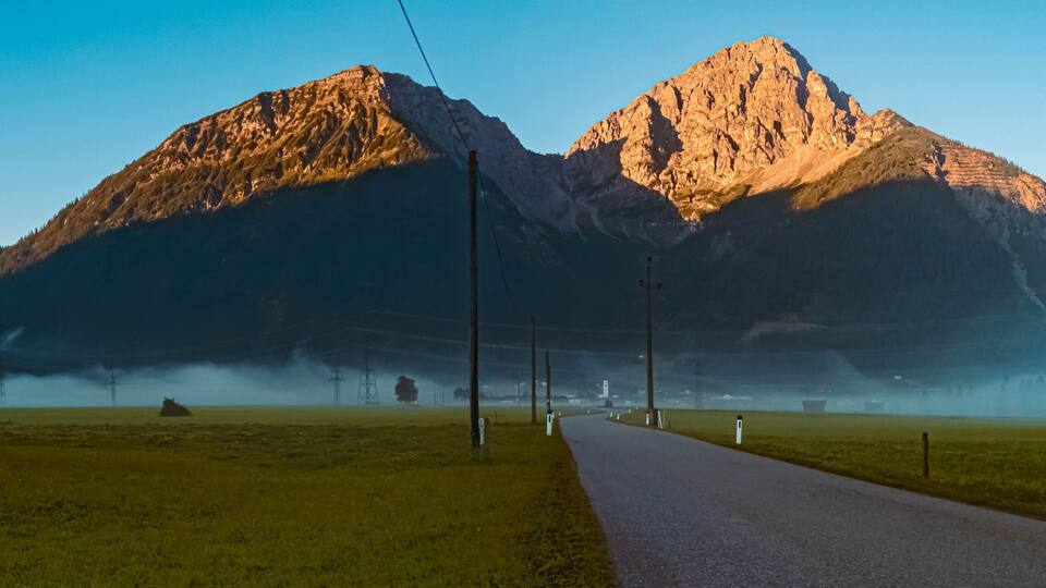 A road leading to a mountain range with a clear sky.