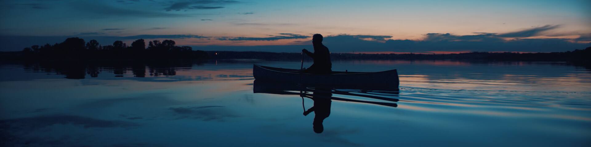 Man canoeing in a traditional wooden boat on a large lake at dawn