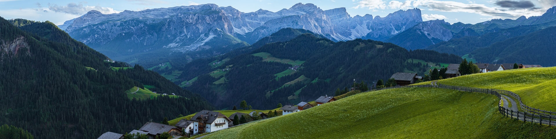 A mountainous landscape with a winding road, green fields, and traditional houses.